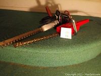 Photo of vintage Sun Beam electric hedge clippers laid flat with blades and red handle visible.