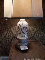 Full view of vintage decorative table lamp with floral ceramic base, round wooden stand, and rectangular fabric shade showing wear