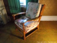 Wood framed chair with fabric cushions showing wear, in indoor setting with green curtains and yellow wall with white baseboard.