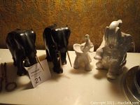 Photo of four elephant figurines: two black elephants with tusks, one small white elephant figurine, and one larger white detailed elephant with one tusk missing.