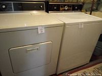 Front and top view of a white Kenmore dryer next to a washer in a basement or laundry room.