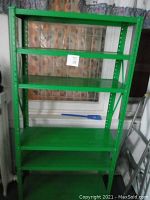 Photo showing a green metal shelving unit with five shelves against a wall.
