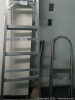 Photo shows two aluminum ladders against a wall, a 6 ft. extension ladder and a smaller step ladder with 2 steps and a safety bar.