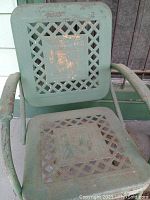 Close-up front view of one retro metal chair showing lattice pattern seat and backrest, chipped green paint, and rust spots.