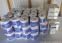 Photo showing stacks of Genuine Joe toilet tissue rolls and boxed Steri-Pad gauze pads on a table.