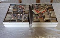 Four white cardboard storage boxes filled with assorted sports trading cards laid out on table, some loose cards on top