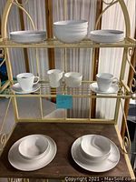 Photo showing set of white Corning Ware Centura dishes including stacked dinner plates, bowls, cups, and cream and sugar on shelves and table.