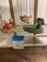 Photo of two Hallmark Peanut Gallery figurines displayed on a metal rack, showing the characters around a pumpkin and Charlie Brown falling with Lucy holding a football.