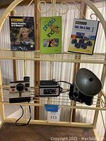 Photo showing three vintage cameras and three photography books on a metal shelf