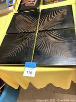 Four separate dark wood planks laid out on a table, showing etched light-colored leaf designs that form a symmetrical pattern when combined.