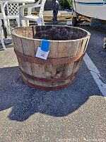 Full view of wooden half wine barrel planter from side showing weathered wood and rusty metal bands, outdoor setting.
