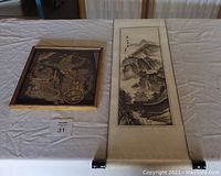 Photo showing the embroidered tapestry framed and the hanging scroll laid out on white cloth.