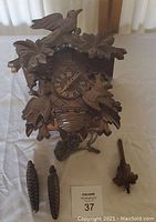 Front view of the wooden cuckoo clock with detailed leaf and bird carvings, showing pine cone weights and pendulum.