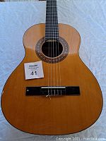 Front close-up view of the Jasmine by Takamine acoustic guitar body showing natural spruce top with mosaic rosette and six strings (one missing) attached to rosewood bridge