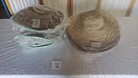 Photo shows a table with stacks of wide-brimmed straw hats in natural light brown and beige colors. Most hats are wrapped in plastic.