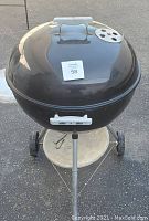 Closed black Weber charcoal kettle BBQ grill from top, showing lid, handle, vent, wheels and ash catcher.