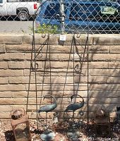Full view of five metal garden decor items in sunlight against brick wall and fence.