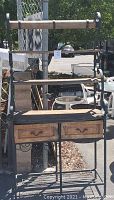 Front view of garden potting bench showing two wooden drawers, solid wood shelves, and black iron frame with decorative scrolls.