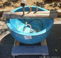 Blue glazed ceramic pot with bamboo water fountain installation on wooden stand with wheels, shown outdoors in sunlight.