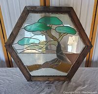 Octagon stained glass window with green tree design and brown wooden frame, displayed standing vertically.
