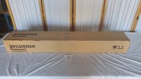 Long cardboard box with Sylvania fluorescent branding on table.