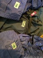 Three REI backpacks stacked showing fabric and REI logo patches; two appear similar child-sized blue backpacks, one adult-sized black backpack partially visible.