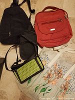 Bird's eye view of four bags including red Bagalinni backpack, black backpack, small black bag, small green woven purse, and two floral printed cloth tote bags