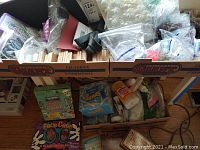 Box containing various craft supplies including craft sticks, bags of glitter, glue, paper molds, rubber stamp sets, beads, and wood blocks