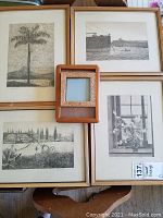Four framed black and white etchings arranged around a small decorative wood frame on a wooden surface.