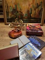 Photo showing the cityscape painting, metal Aspen leaves sculpture, copper enamel bowl plate, Dragons of Pern board game, and signed books stacked
