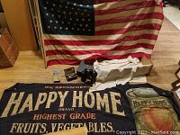 Photo showing 46 star American flag, Happy Home Peaches advertising banner, and fabric with stencils, all arranged on wooden floor.