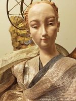 Close-up of angel face showing detailed painted features, light skin, reddish hair, and delicate expression.