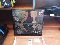 Full view of the black enamel wall panel with silver metal shapes and the four small cast sculptures on cardboard