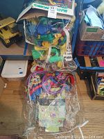 Clear plastic bag containing multicolored plastic pieces for marble works toy set, shown on wooden floor with surrounding items.