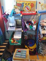 Overview of storage rack containing various toys including label maker, dolls, train box, and assorted clothing.