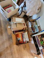 Boxes containing numerous children's books stacked and laid out on a wooden floor, including some packed for shipping or moving.