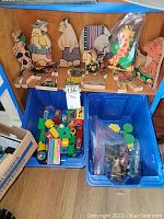Image showing various handmade wooden animal blocks arranged on a wooden shelf, plastic bins below with MagnaToys building pieces and a bag of small animal figures.
