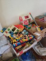Overview of boxes containing various Fisher-Price Little People playsets including barn, house, slide, and many figures and accessories.