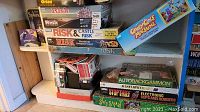 Shelf with various board games layered and stacked including Risk, Splendor, Goofy Golf Machine, and Orion combat game.