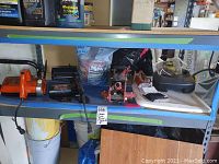 Photo shows two chain saws on a blue metal shelf with other tools and materials. Orange McGraw-Edison 10" chain saw on left, red and black other chain saw on right with floor jack and miscellaneous items.