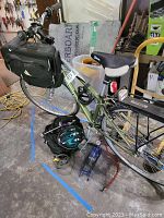 Overall view of green Novara Corsa bike with front and rear bags, helmet, lock and pump on workshop floor