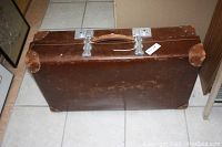 Closed vintage leather suitcase showing brown leather exterior with metal clasps and worn leather handle.