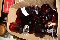 Box filled with various red glass drinkware including tall tumblers, short tumblers, and goblet glasses with clear stems, all vintage Luminarc and Verrerie D’Arques France.