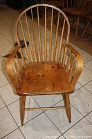 Single captains chair on tile floor showing spindle back, armrests and saddle seat.