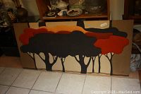 Full view of the quilted textile artwork showing stylized trees with layered fabric in orange, black, and beige tones, framed.