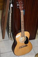 Full view of the small-bodied acoustic guitar showing natural wood top, black pickguard, and six strings.