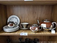 Photo of the full tea set displayed on a wooden shelf including teapot, creamer, sugar bowl, teacup and saucer, and six side plates.