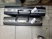 Top view of two closed briefcases on tiled floor, black and gray colors with metal locks and handles.