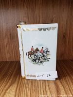 Front view of the Limoges brandy flask showing the hunting scene with riders on horses and dogs, white porcelain and gold detailing.