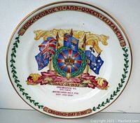 Front view of the commemorative plate showing the colorful flag motif with wreath and crown, text around the rim indicating the coronation event and date.